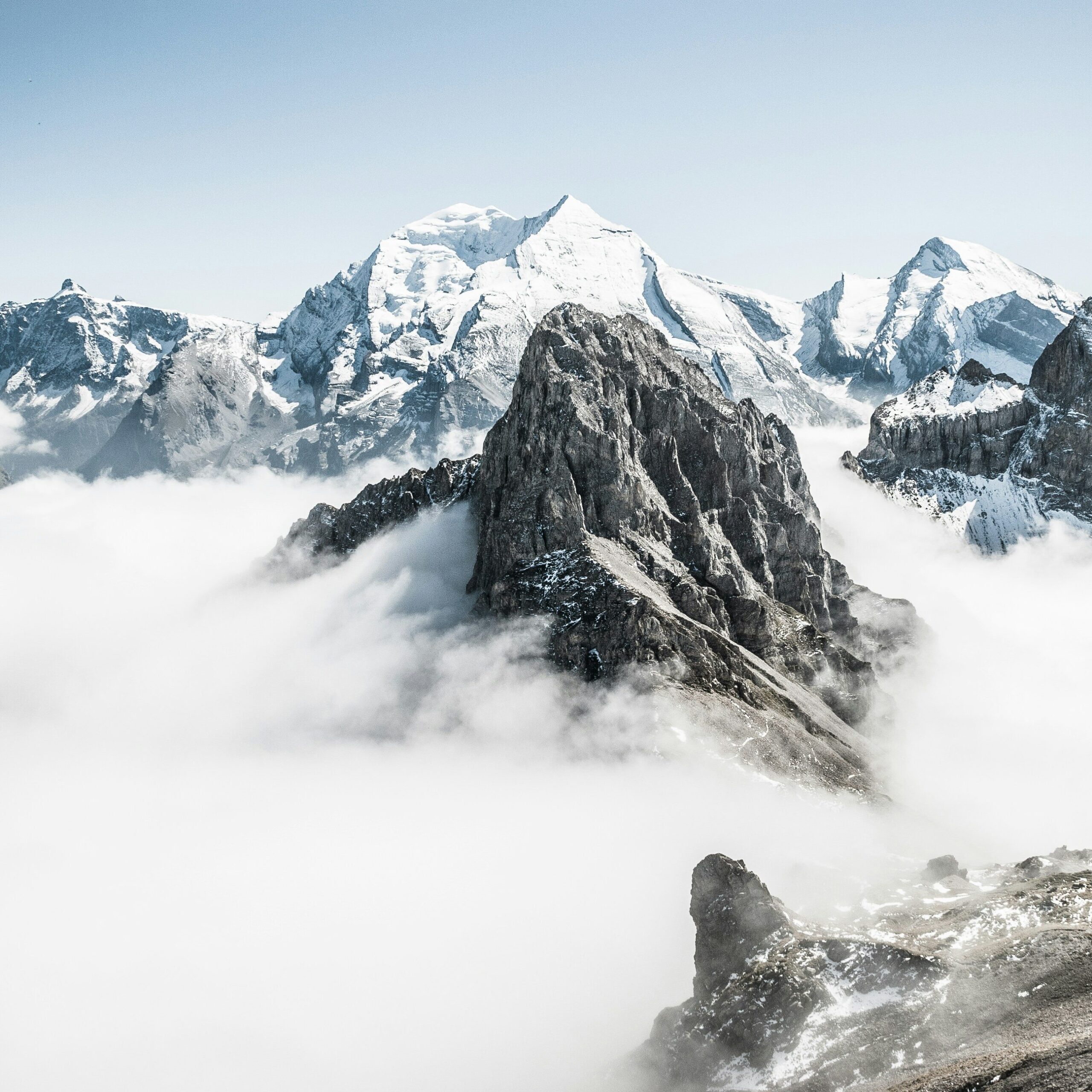 Snow-covered mountains surrounded by clouds under a clear blue sky