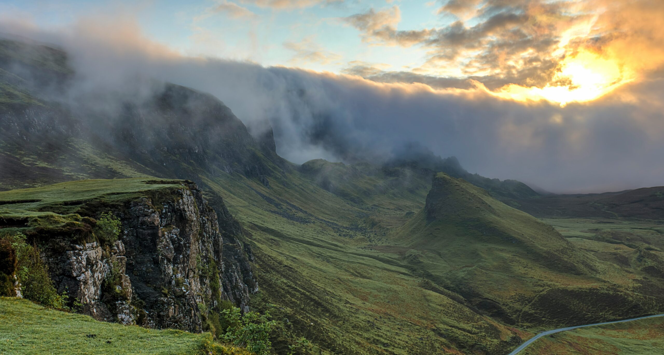Sunrise over misty green mountains and cliffs with fog.