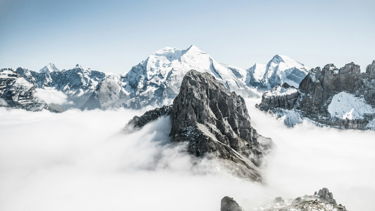 Snow-covered mountains rising above dense clouds, creating a serene and majestic landscape.